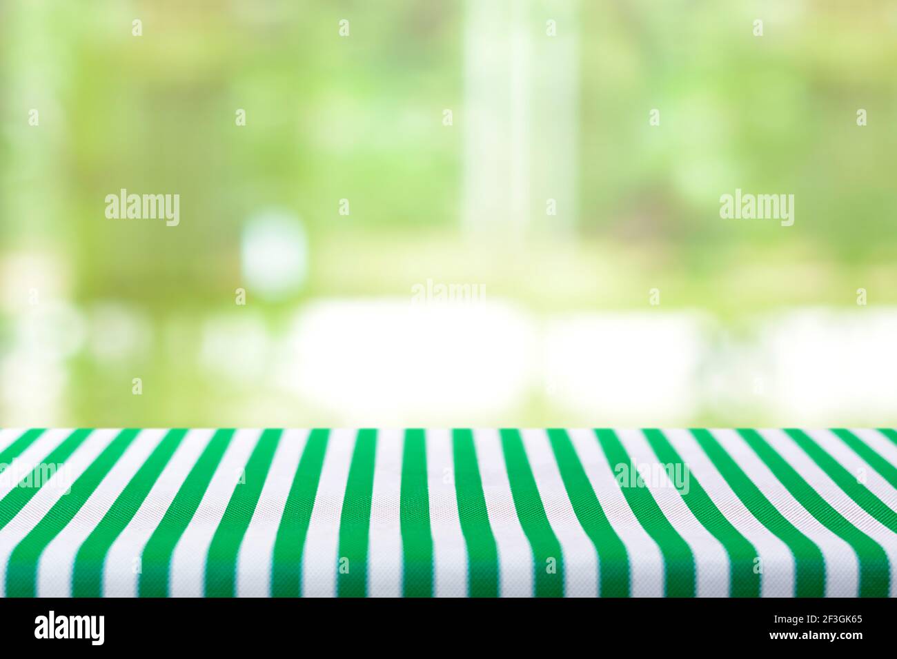 Tavolo coperto con tovaglia striata su verde astratto sfocato sfondo - può essere utilizzato per montaggio e visualizzazione di alimenti o prodotti Foto Stock