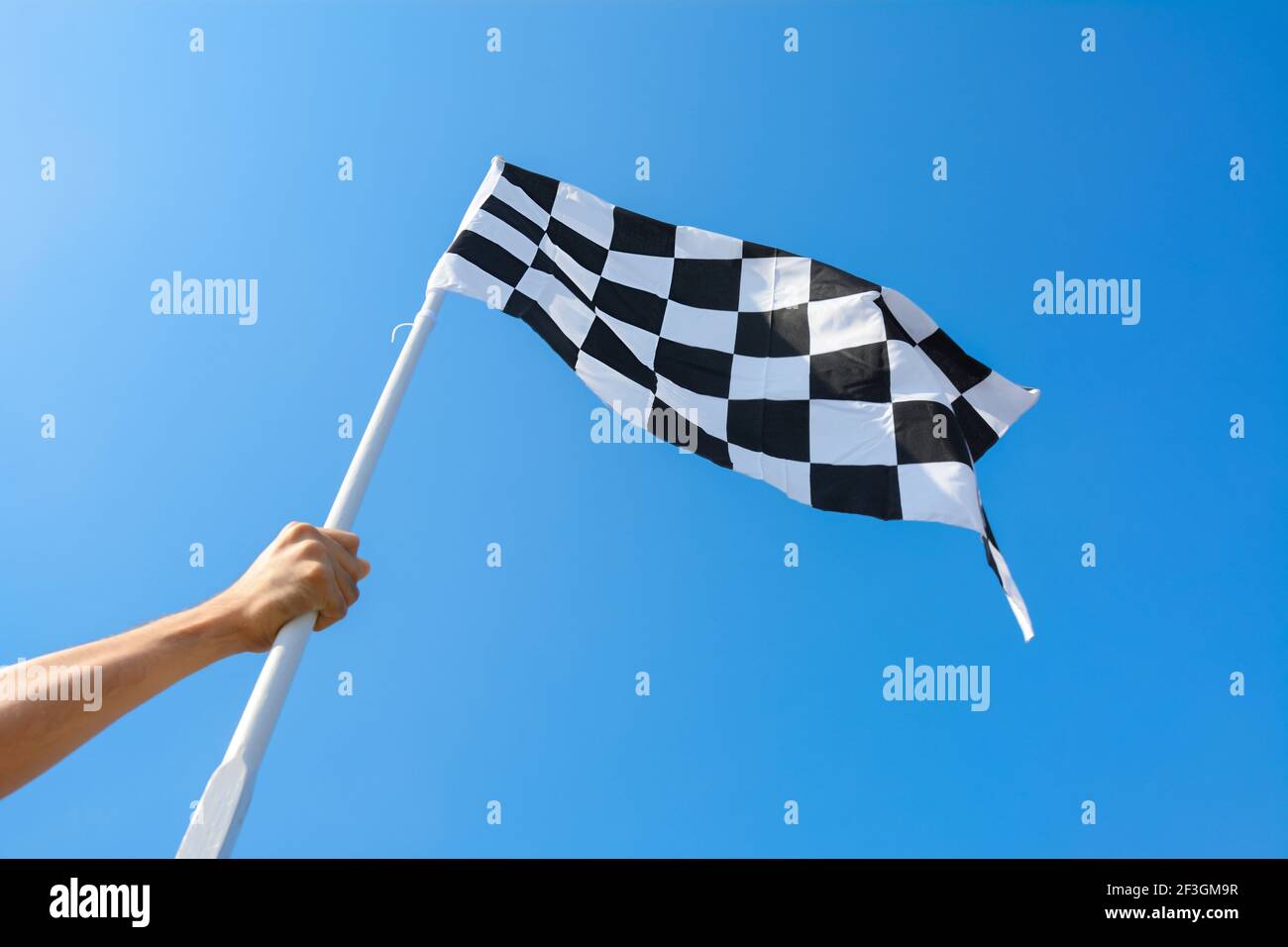 Mano che tiene bandiera a scacchi su sfondo blu cielo Foto Stock