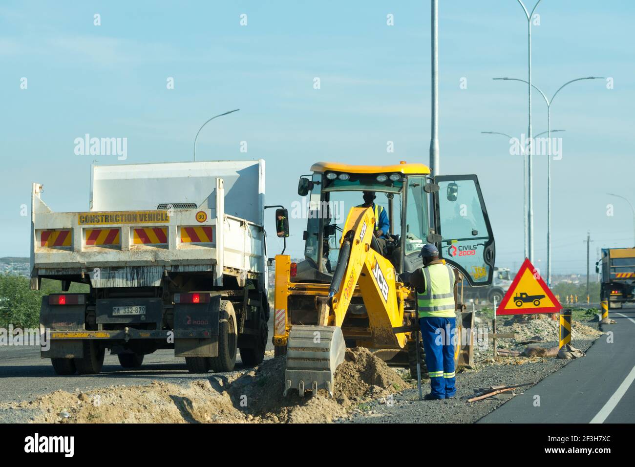 Lavori su strada, costruzione di strade, riparazioni stradali in primo piano con persone, dipendenti, lavoratori che scavano un fossato o una trincea con un bulldozer a Città del Capo, Sudafrica Foto Stock