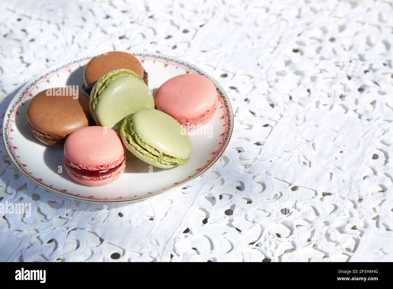 Biscotti macaron in colore rosa, verde e marrone con piattino in ceramica e tovaglia bianca ricamata Foto Stock