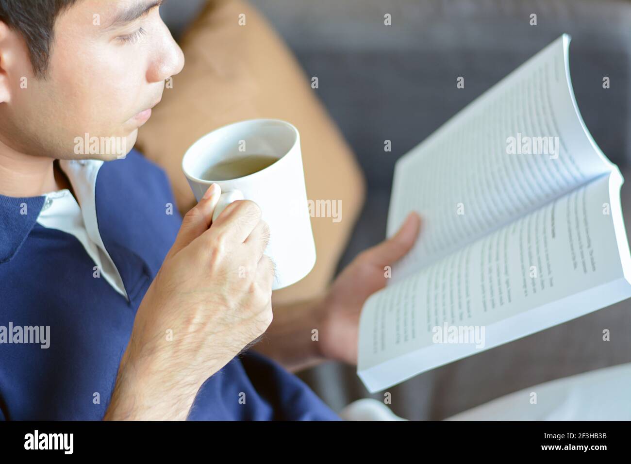 Un libro di lettura dell'uomo con la tazza calda del tè in un altro mano Foto Stock