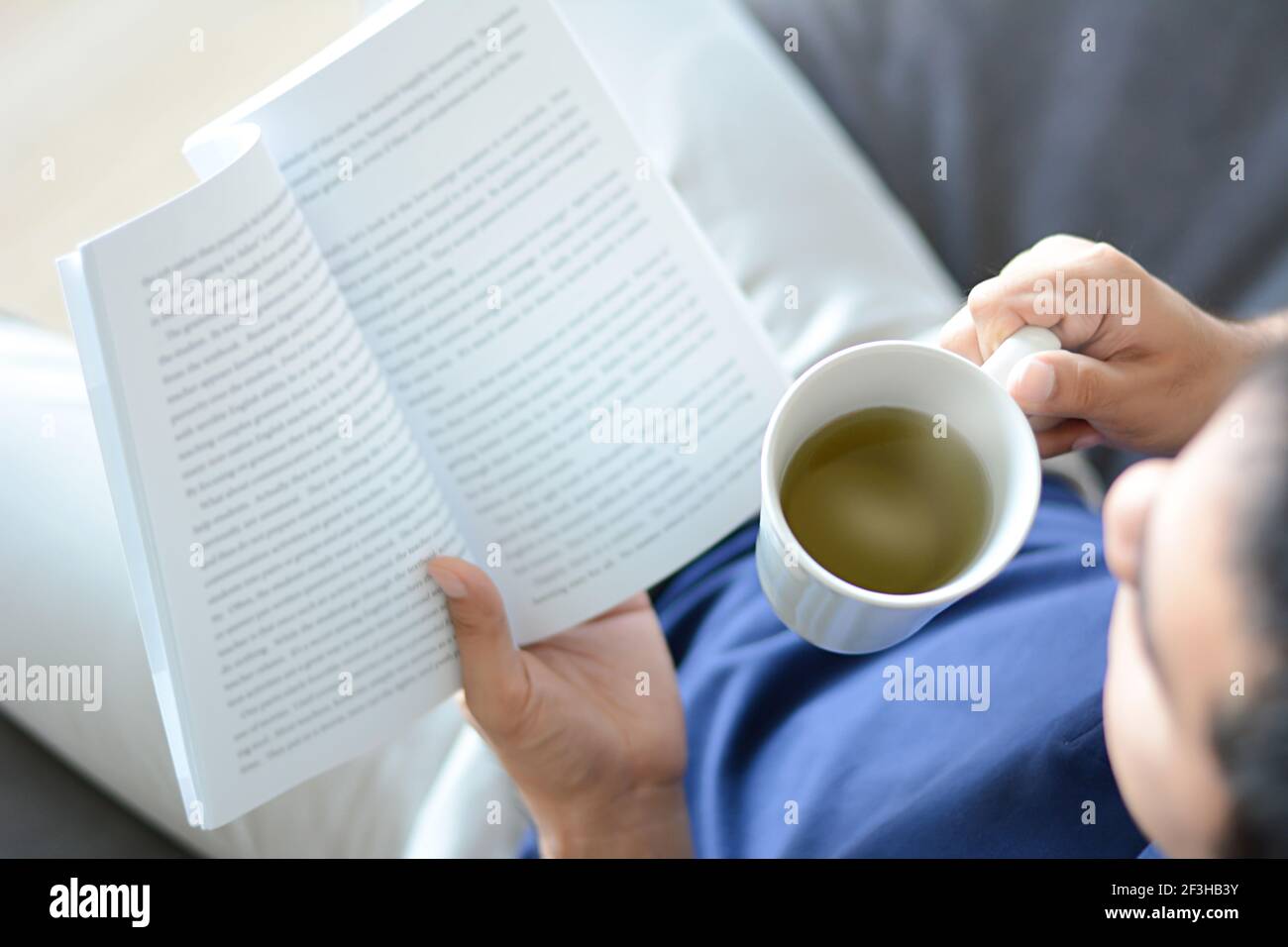 Un libro di lettura dell'uomo con la tazza calda del tè in un altro mano Foto Stock