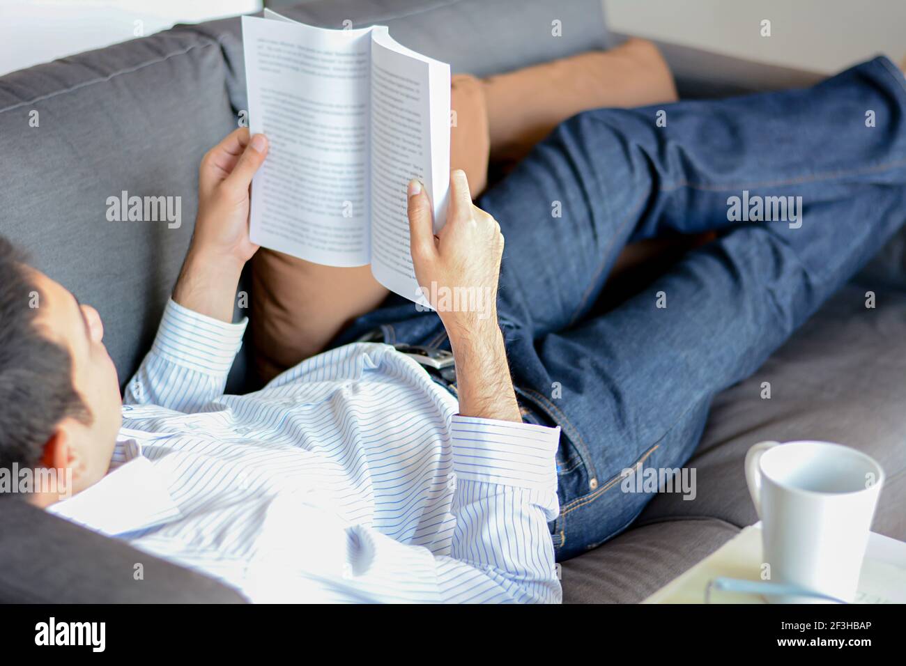 Un uomo che legge libro mentre si sdraiò sul divano Foto Stock