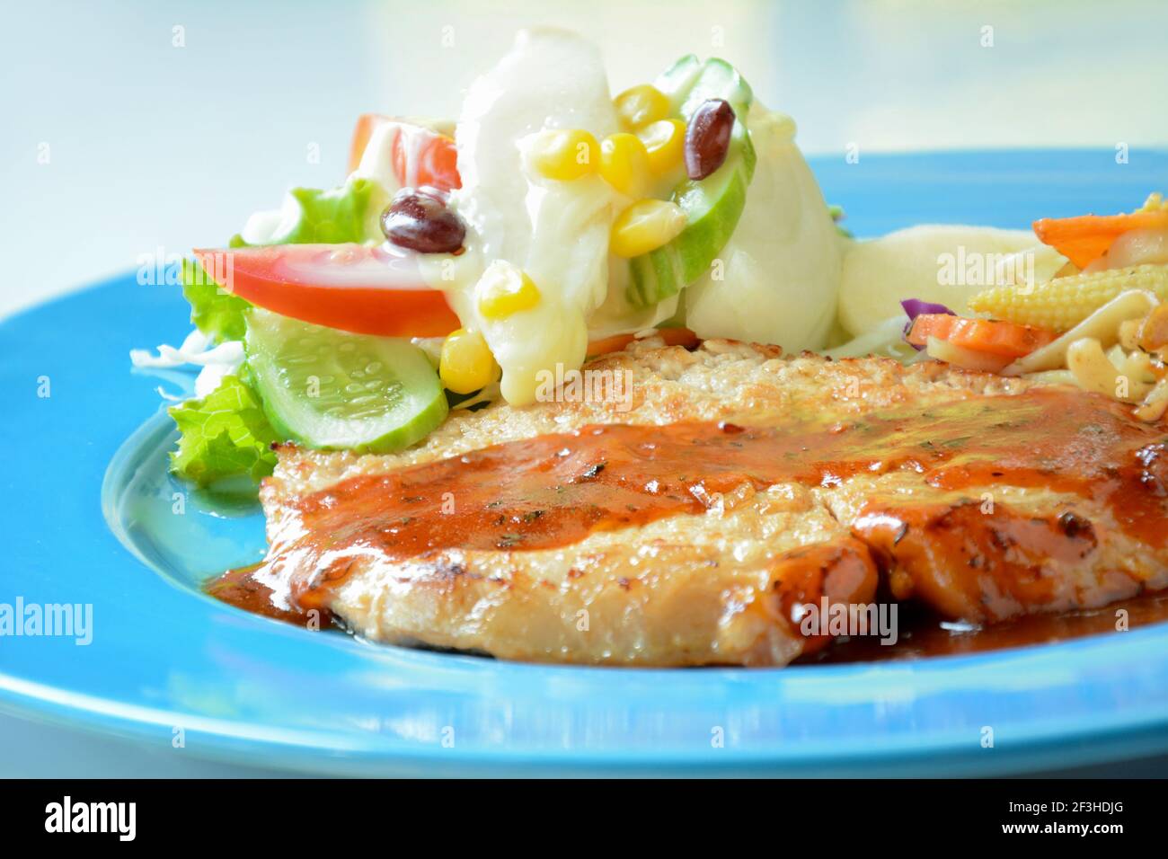Pan bistecca di maiale fritto con insalata mista di verdure su colorato piastra blu Foto Stock