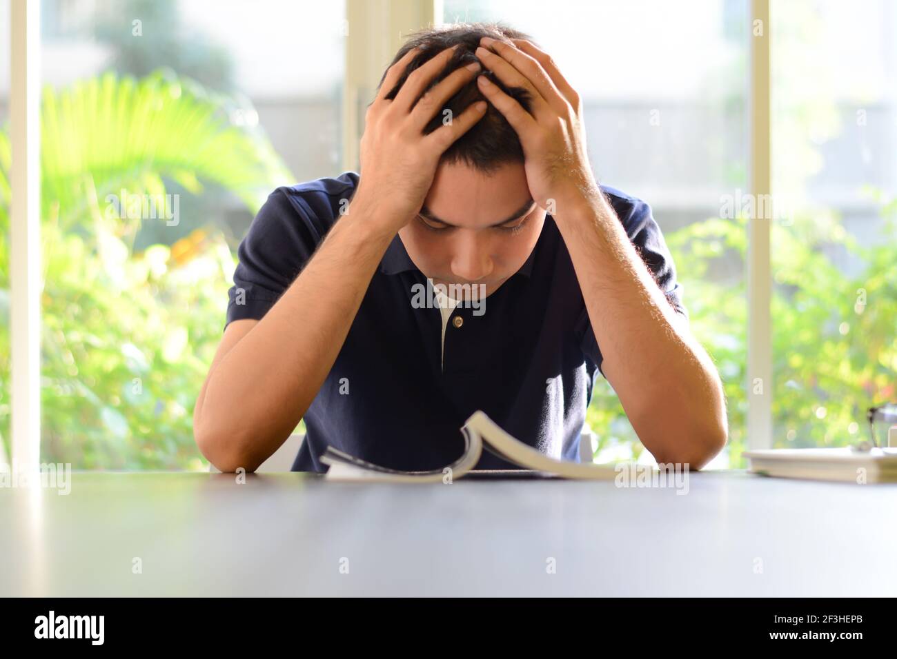 Giovane uomo che tiene la testa con le mani, stanco di leggere e studiare Foto Stock