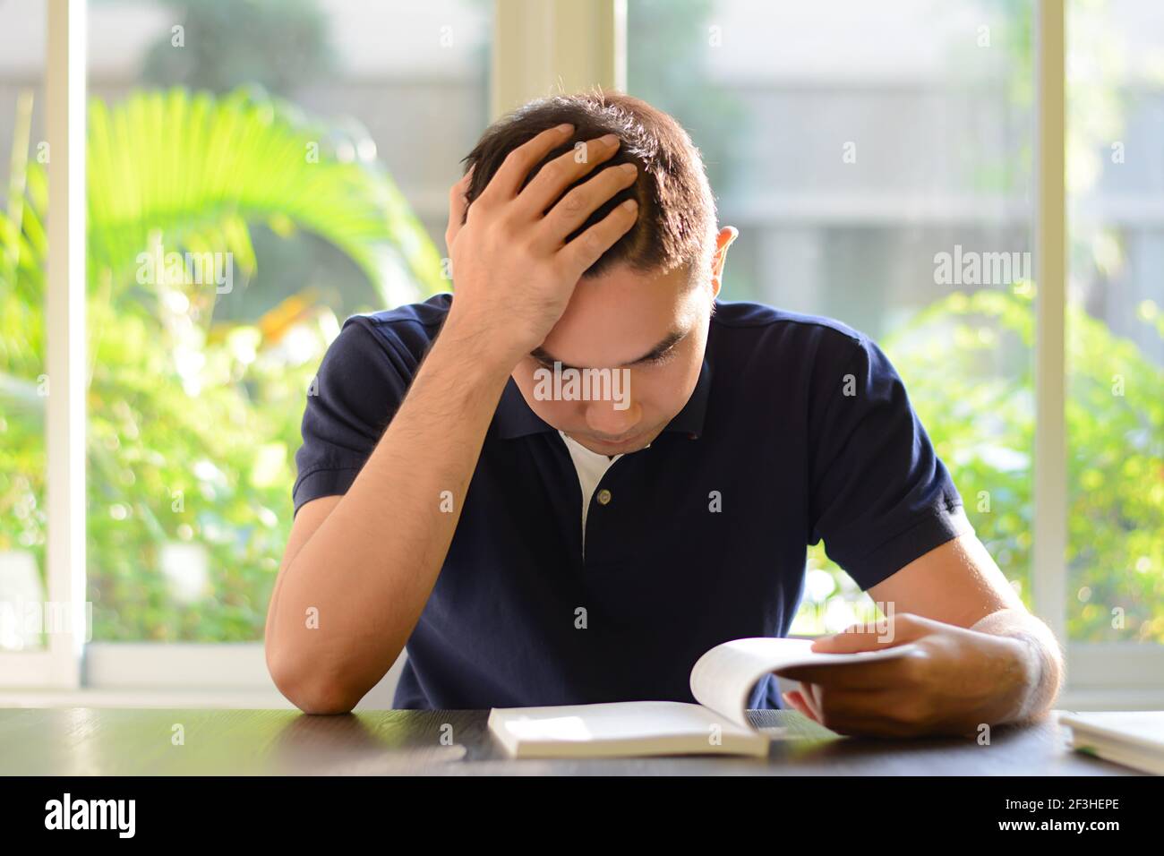 Libro di lettura del giovane uomo con la mano sulla sua testa Foto Stock