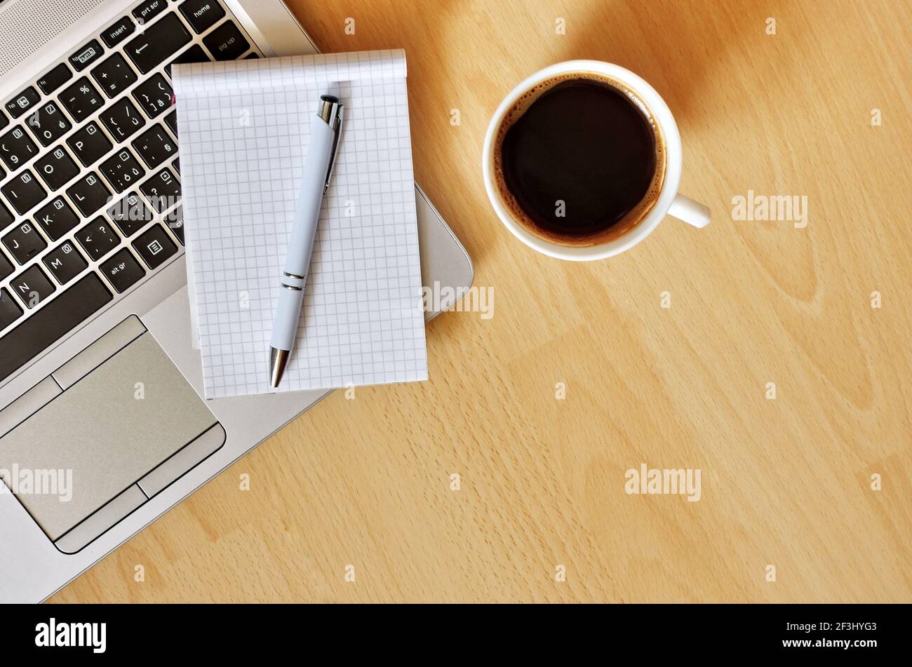 Computer portatile con tazza da caffè, notebook e penna su sfondo di legno, concetto per l'ufficio domestico. Concetto aziendale. Lavoro da casa. Scrivania da ufficio. Foto Stock