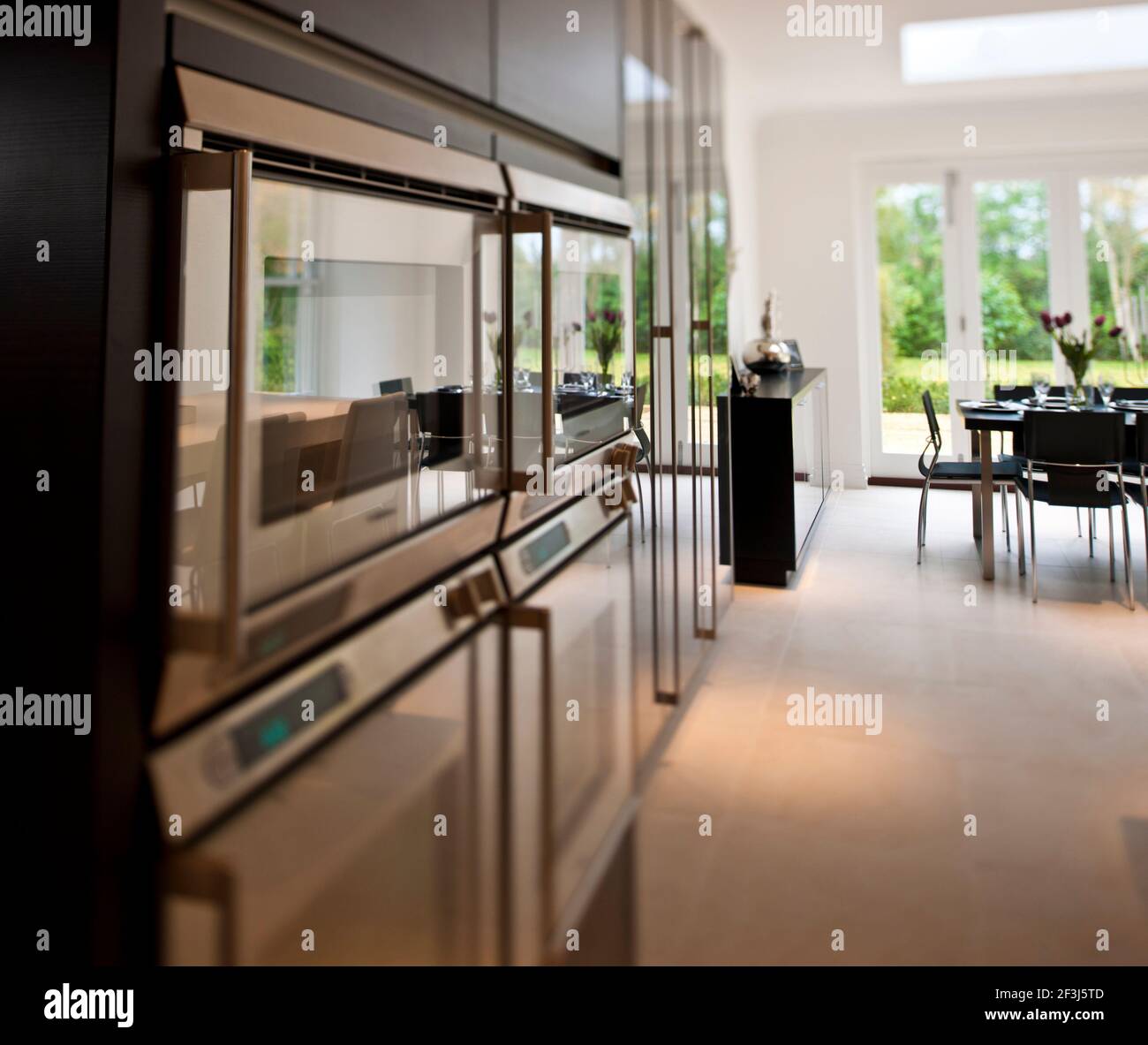 Vista di dettaglio dei riflessi nelle porte di vetro dei forni in una cucina minimalista / sala da pranzo, in una nuova casa di costruzione in Virginia Water, Surrey, con din Foto Stock
