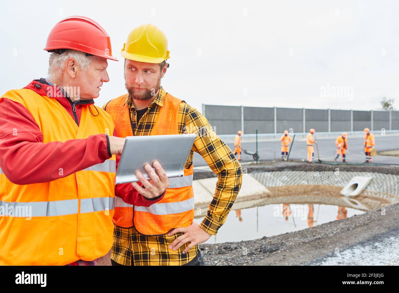 Due operai edili con il sito di costruzione del controllo dei PC tablet di costruzione stradale con scavo Foto Stock
