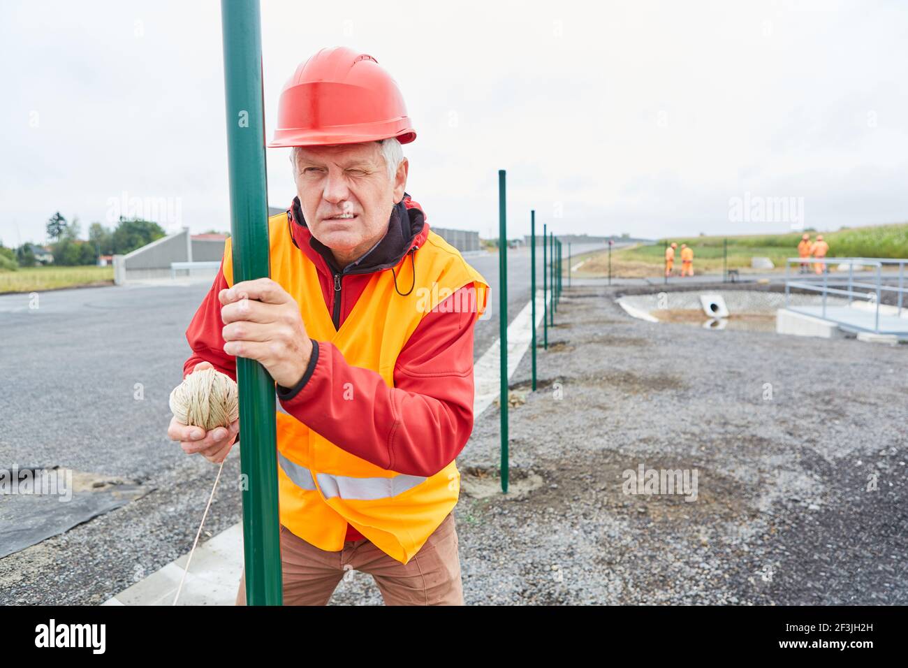 Lavoratore di costruzione con linea guida alla costruzione di recinzione sul cantiere nella nuova area di sviluppo Foto Stock