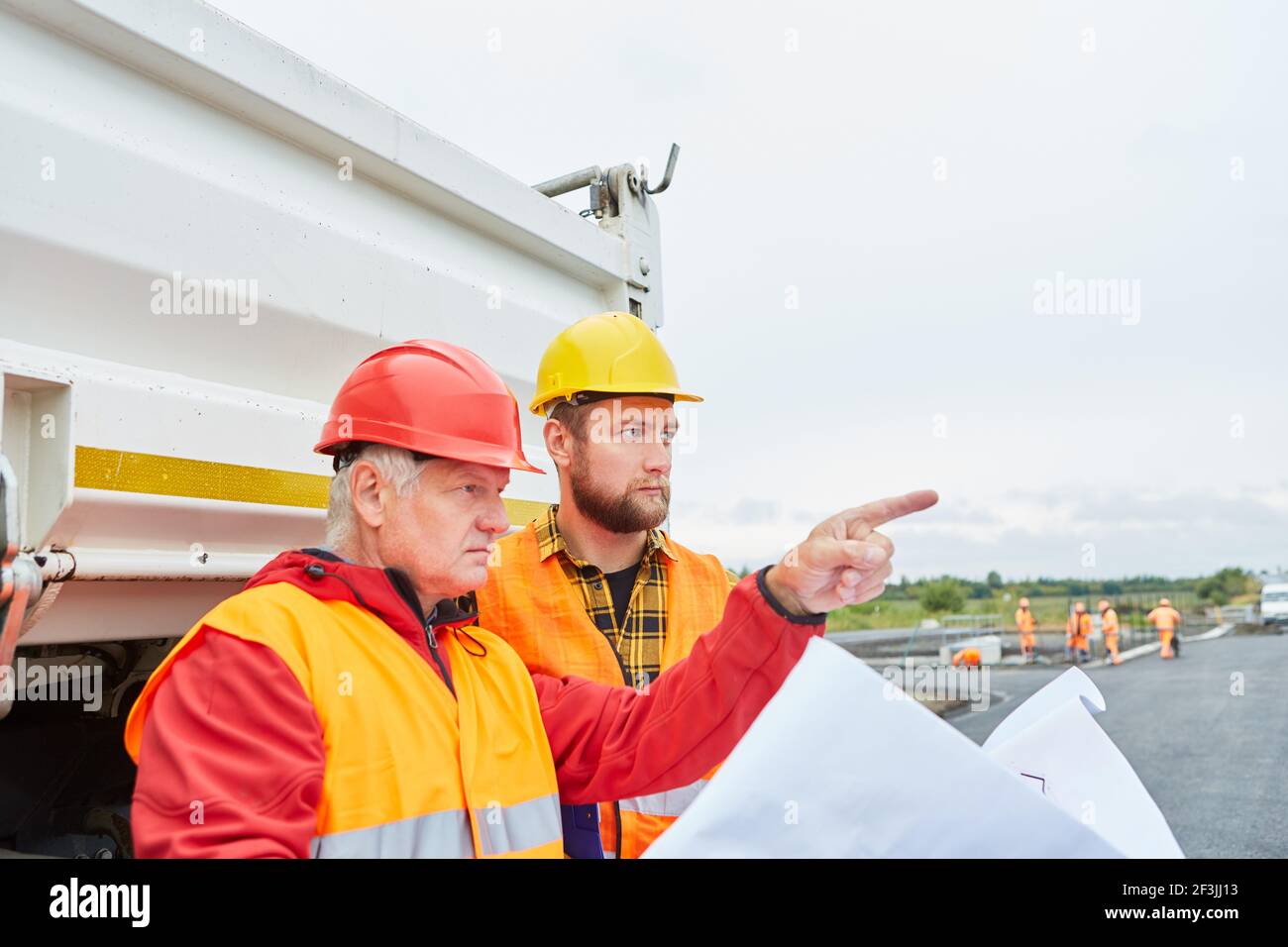 Operaio di costruzione e architetto con disegno di costruzione per la costruzione della casa in un cantiere con camion Foto Stock