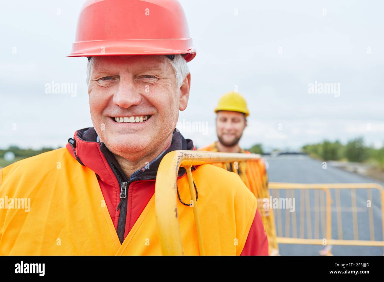 Sorridente lavoratore e collega trasportano barriere per la costruzione di strade sicurezza Foto Stock