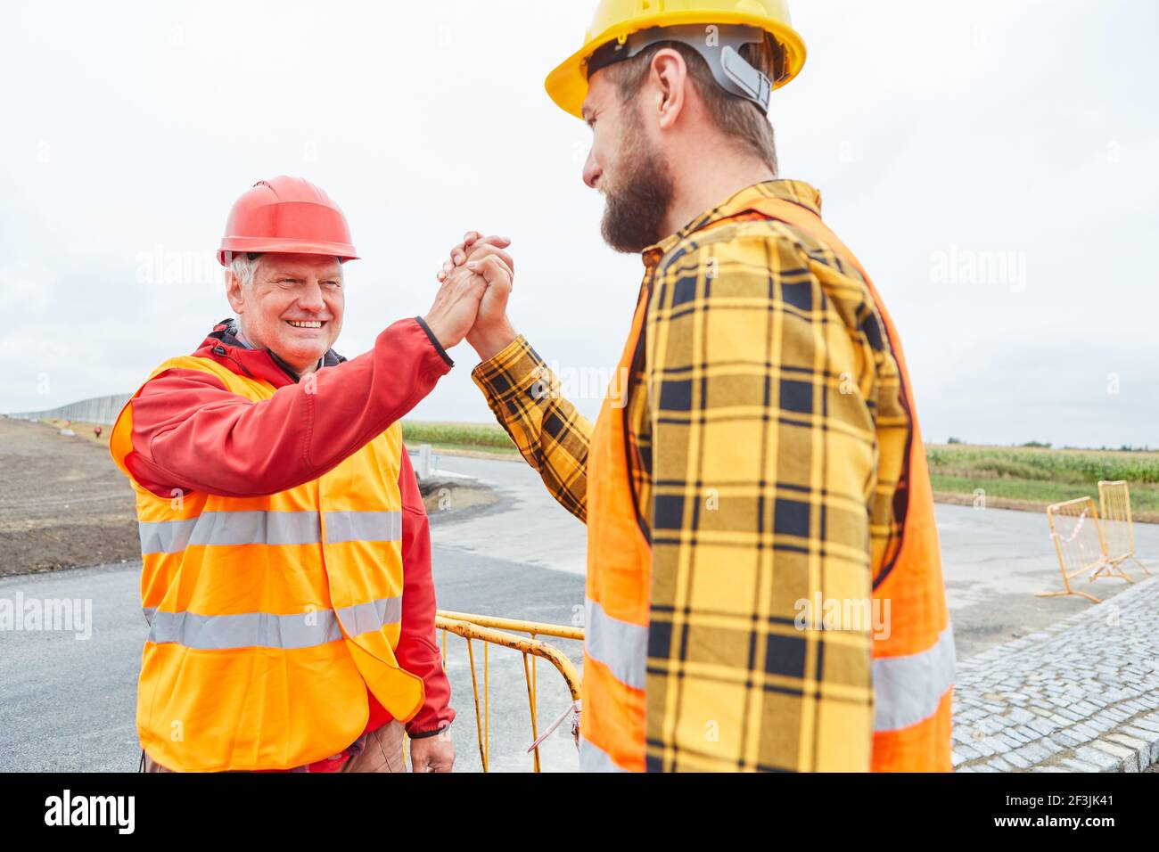 Due lavoratori della costruzione di strade celebrano il successo con la stretta di mano Foto Stock
