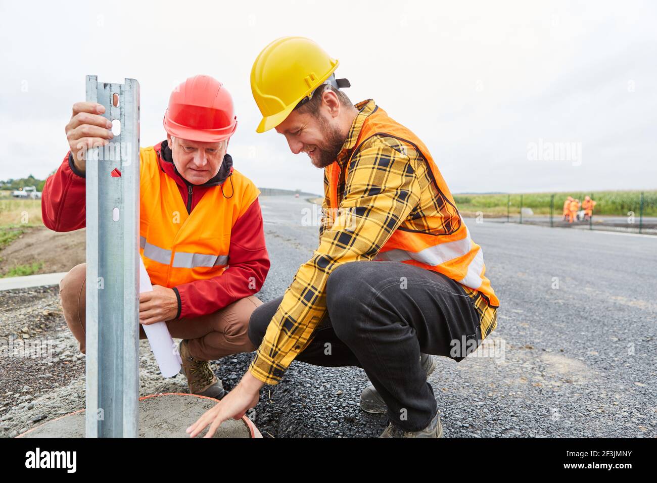 Due addetti alla costruzione controllano la fondazione per le guide di protezione sul cantiere sito di costruzione stradale Foto Stock