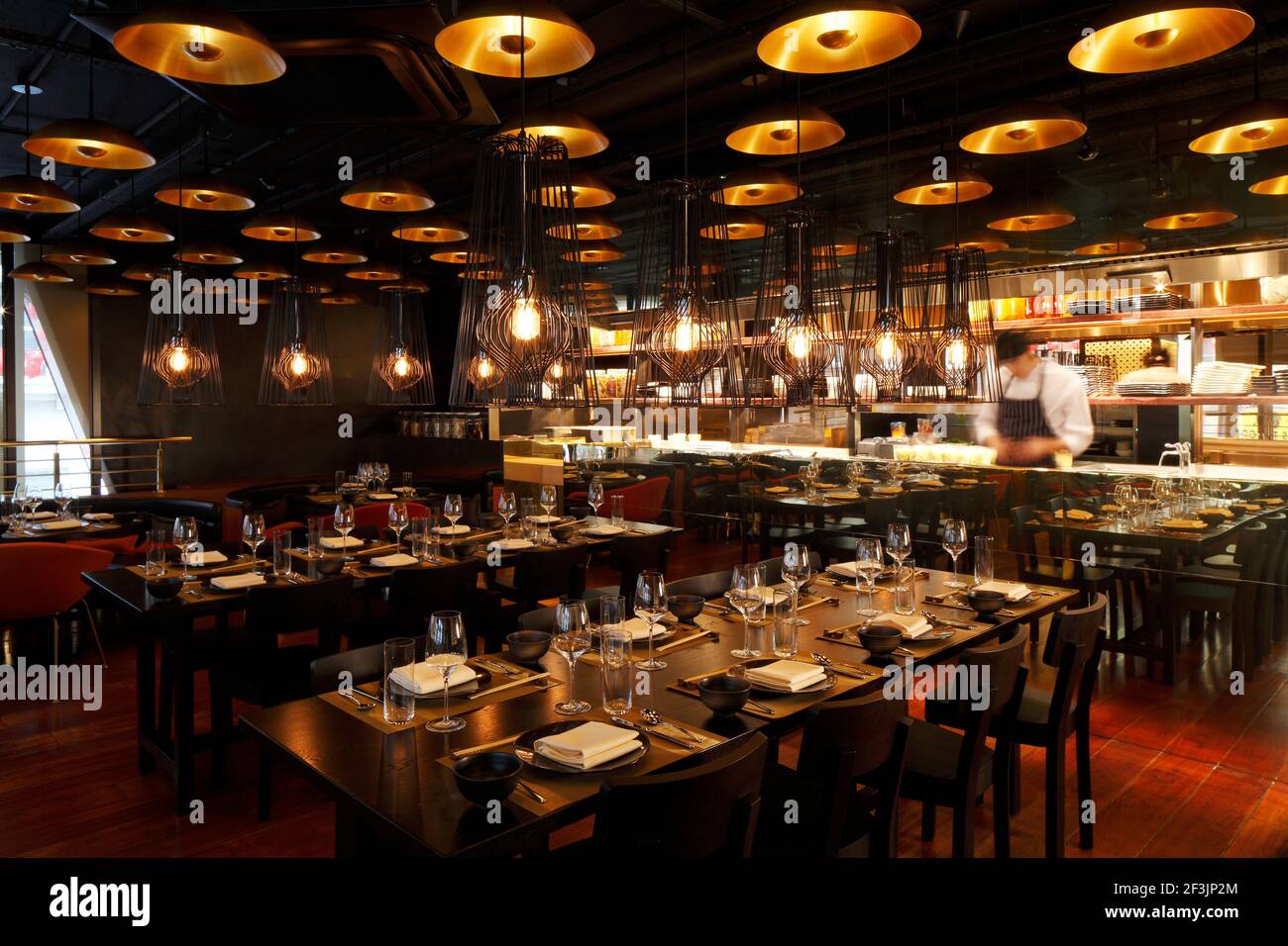 Tavoli dello chef. Chef al lavoro dietro il bancone. 2 grandi tavoli posti sotto gli arredi in stile wok dorato | | Designer: Concrete (Amsterdam) Foto Stock