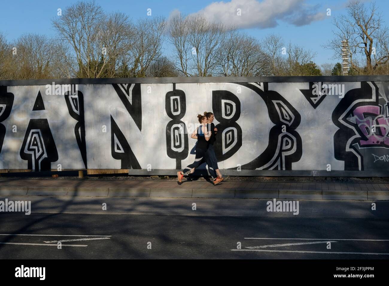 Due femmine che corrono su una strada di Bristol oltre i graffiti. Foto Stock