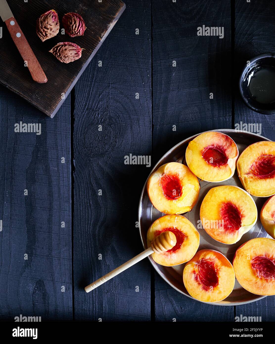 Pesche tagliate succose con miele vicino al coltello e semi di pesca su tavolo scuro in legno in cucina a casa di campagna Foto Stock