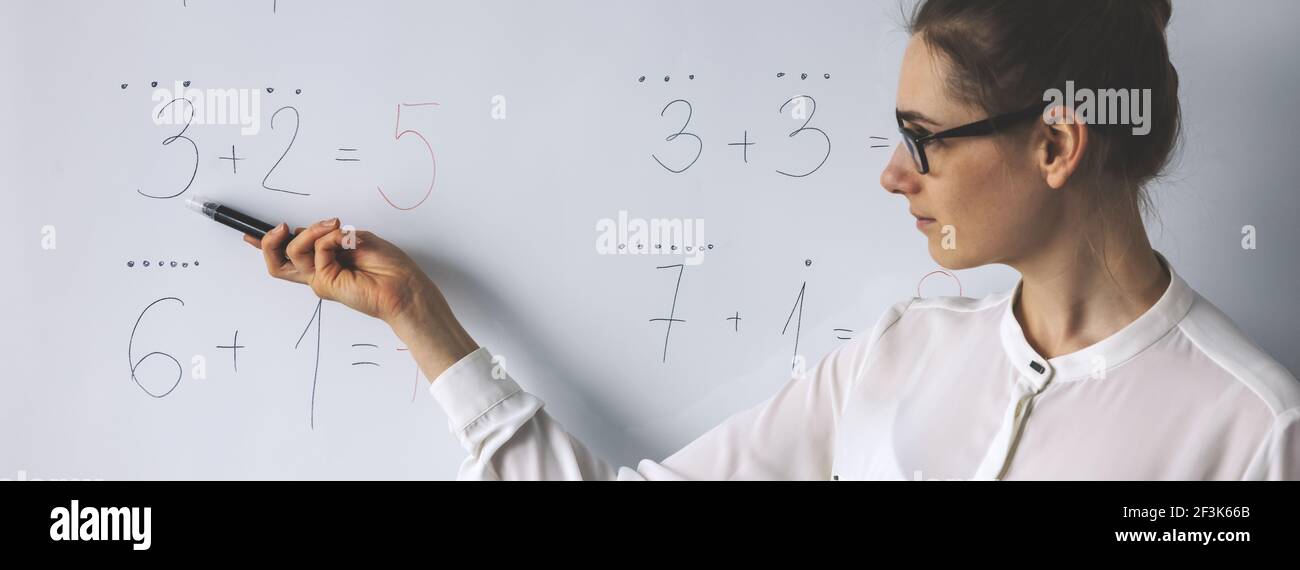 lezione di matematica - insegnante che mostra semplici equazioni matematiche sulla lavagna in classe Foto Stock