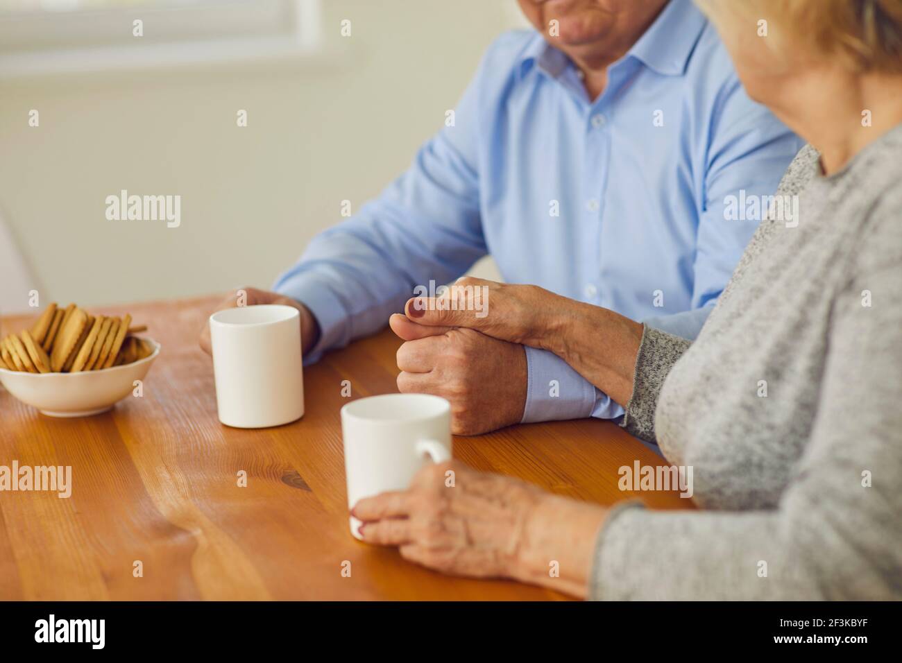 Primo piano in mattinata la coppia anziana che tiene le mani seduti al tavolo e bere il tè. Foto Stock