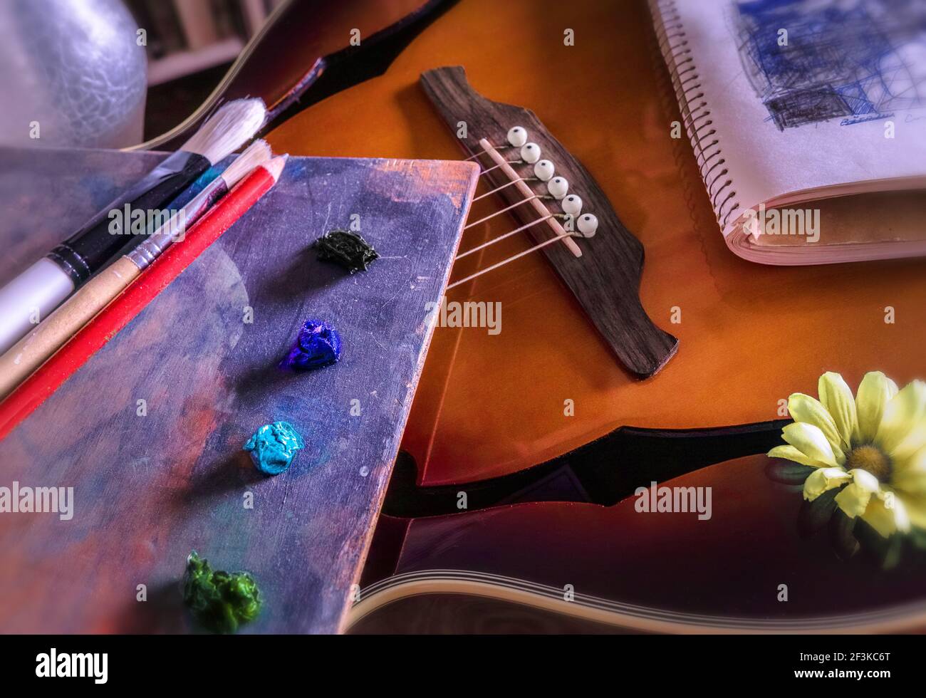 Una tavolozza di un pittore, una chitarra acustica, colori a olio, una margherita gialla (artificiale), pennelli e una penna, un libro di schizzi. Lo studio dell'artista. Foto Stock