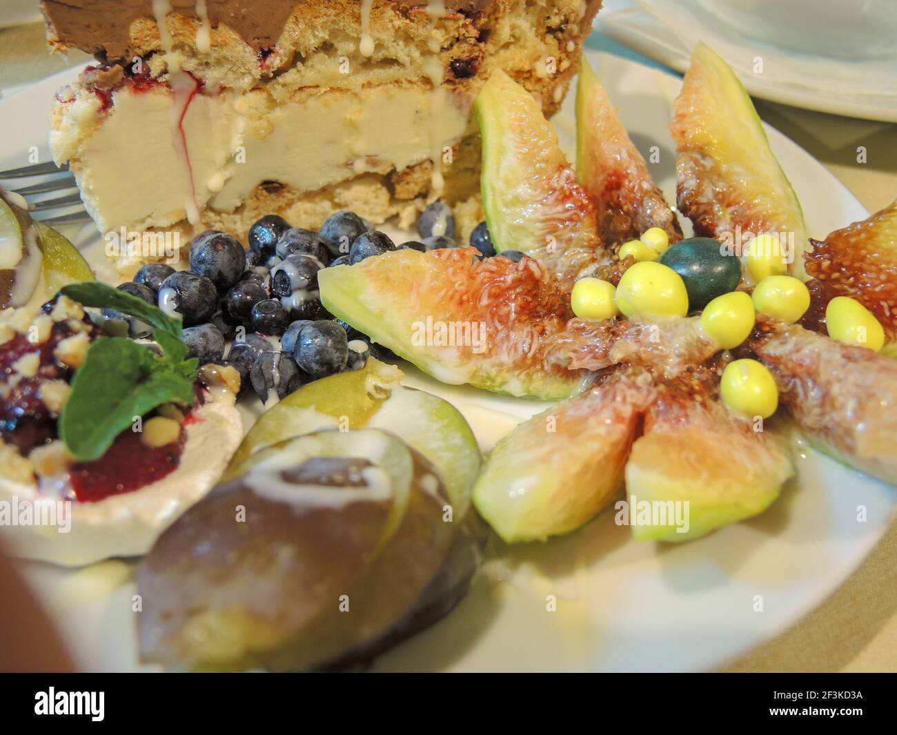 Un piatto di fico tagliato fresco, mirtilli e altri frutti con un pezzo di torta Foto Stock