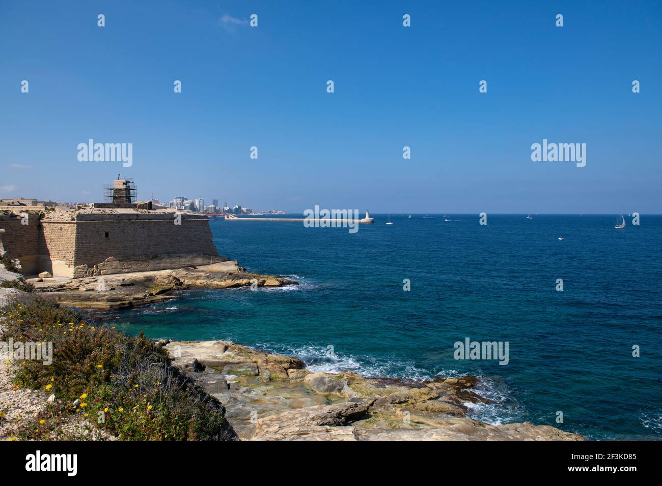 Costa maltese con vista sull'acqua di mare di Sant'Elmo e sul faro di Sant'Elmo, vista dal forte di Ricasoli Foto Stock