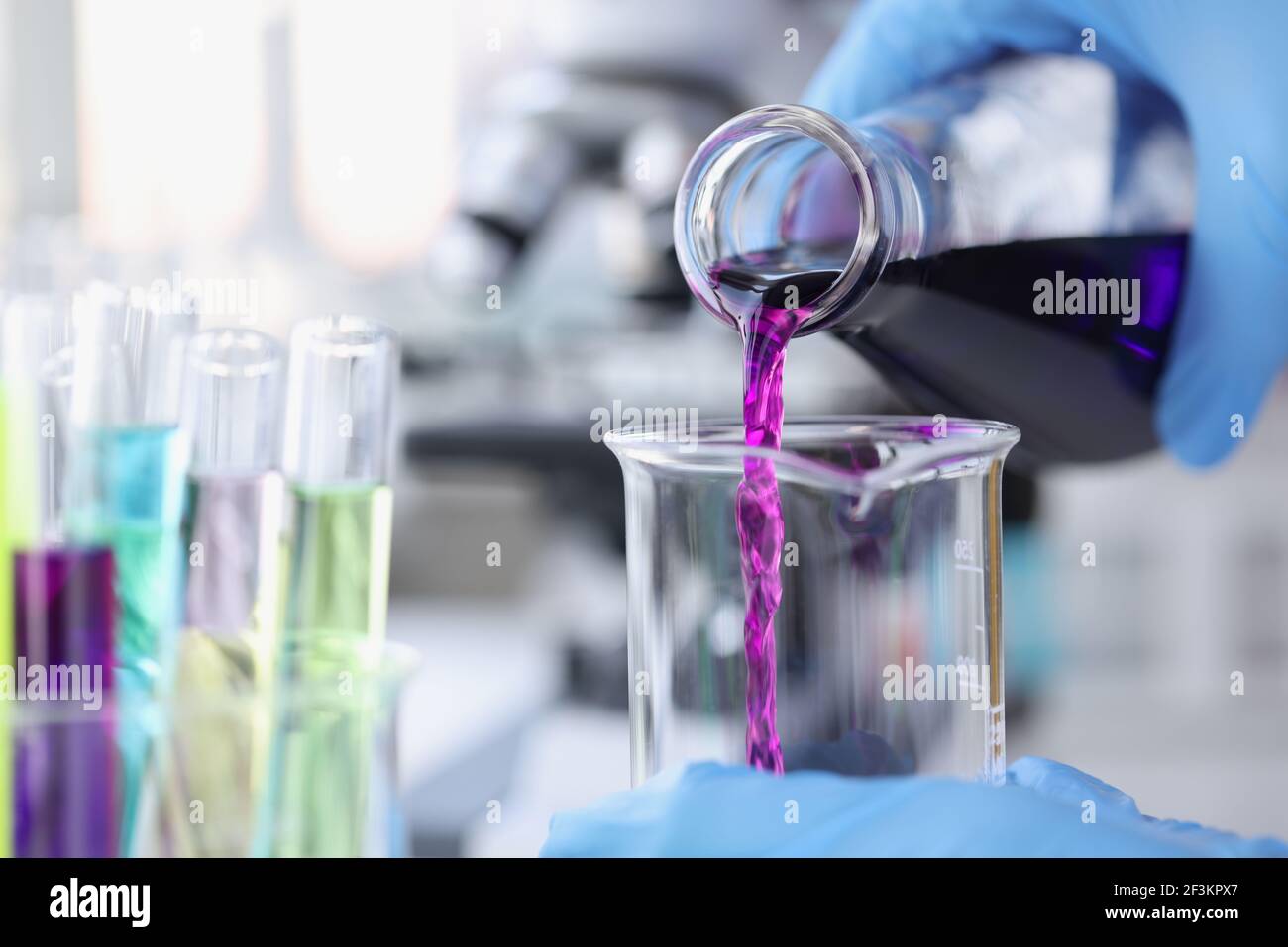 Chimico scienziato che versa liquido rosa nella provetta in laboratorio primo piano Foto Stock
