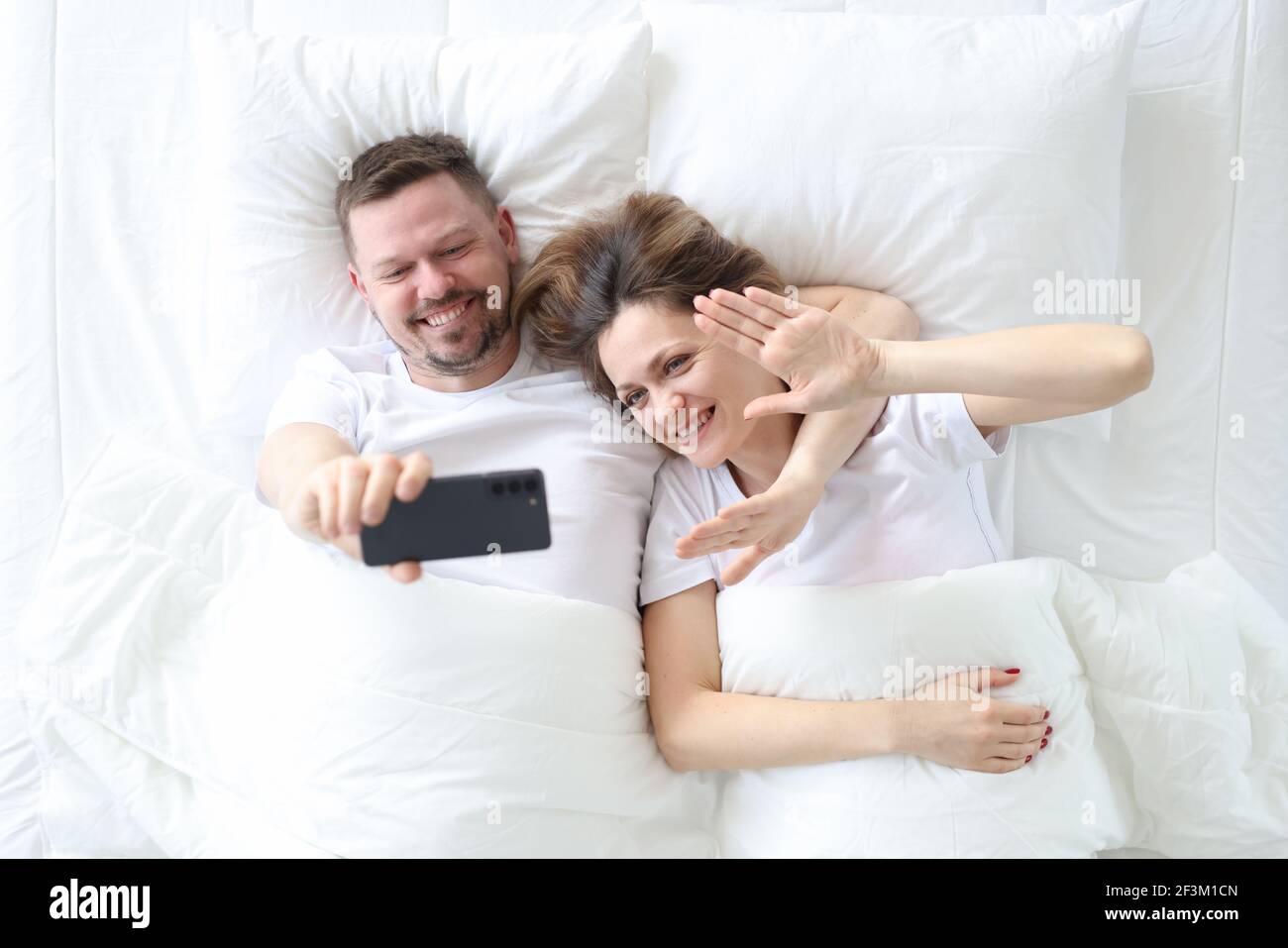 Uomo e donna sdraiati a letto e prendendo il top selfie visualizza Foto Stock