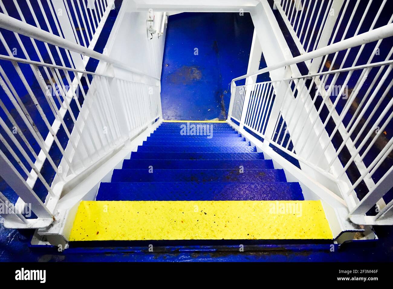 Scala in acciaio blu e giallo dipinta di luce sul traghetto Foto Stock