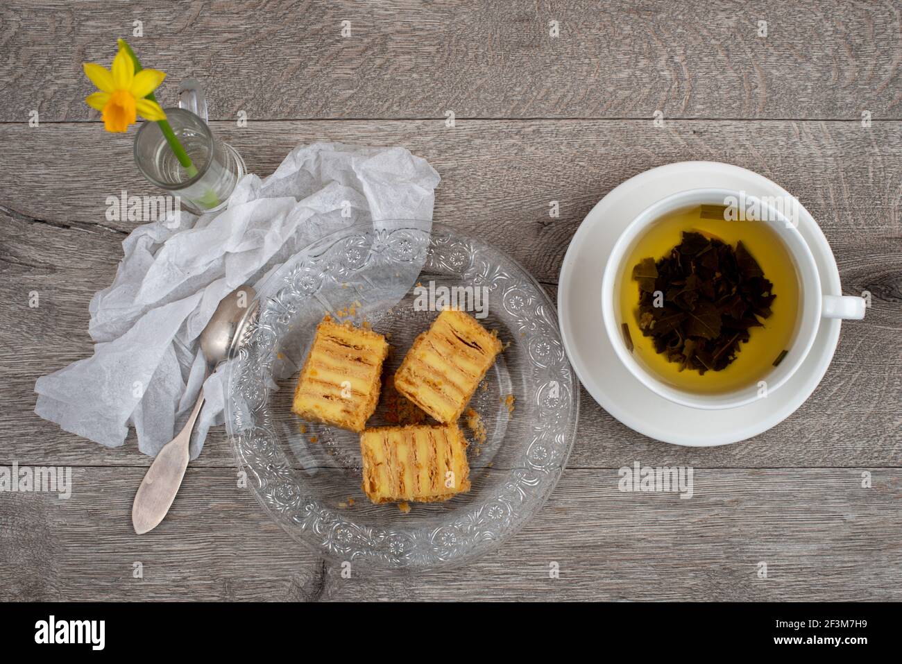 Composizione della torta Napoleonica, tazza di tè verde e fiore di Daffodil. Primo piano, vista dall'alto. Foto Stock
