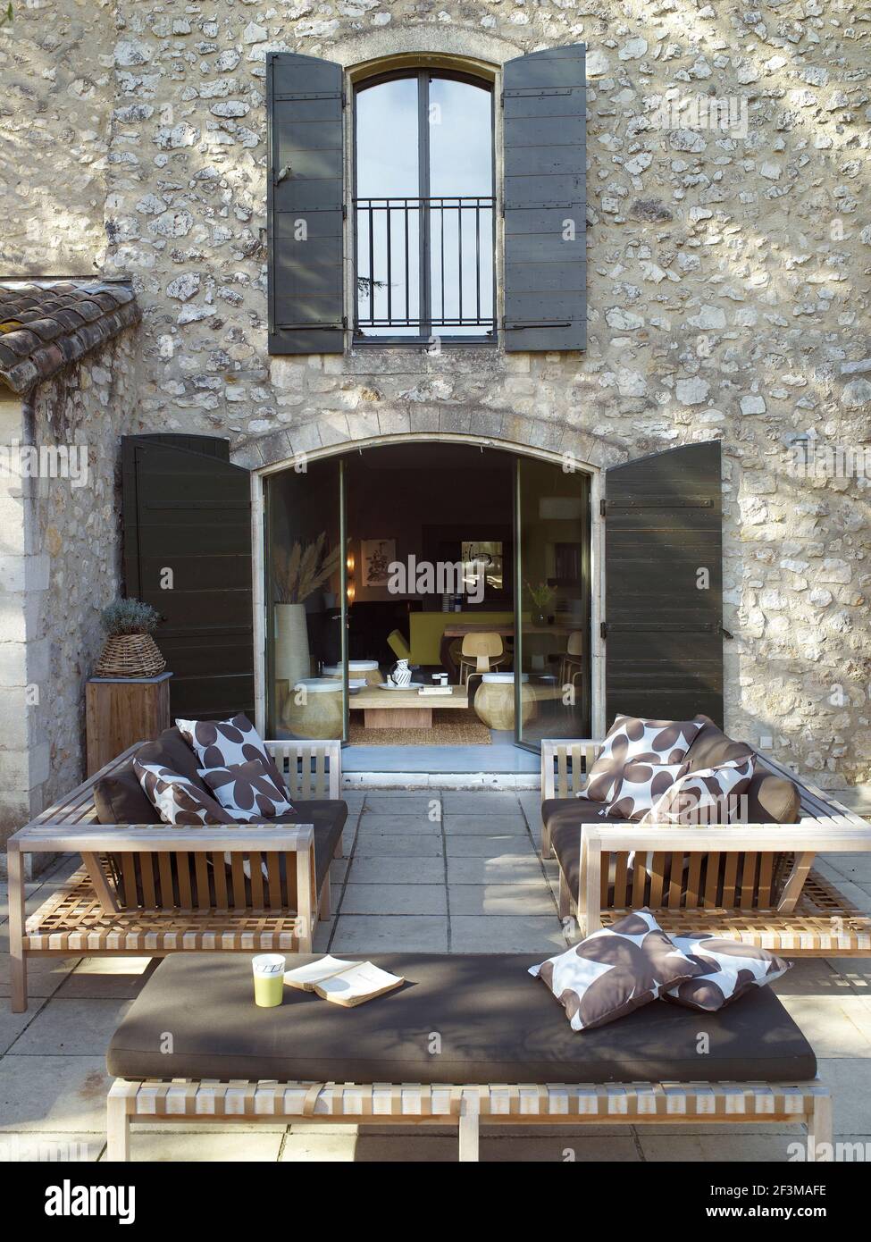 Due divani e un lettino sul patio accanto alle porte del patio con persiane in legno che conducono alla villa francese. Foto Stock