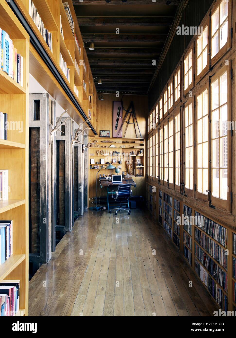 Lungo corridoio in legno con finestre, con libri e DVD con scrivania e sedia in casa residenziale spagnola. Foto Stock