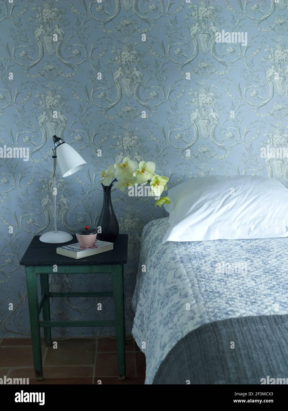 Carta da parati a motivi in colore coordinato camera da letto con comodino, vaso con fiore e lampada, Francia Foto Stock