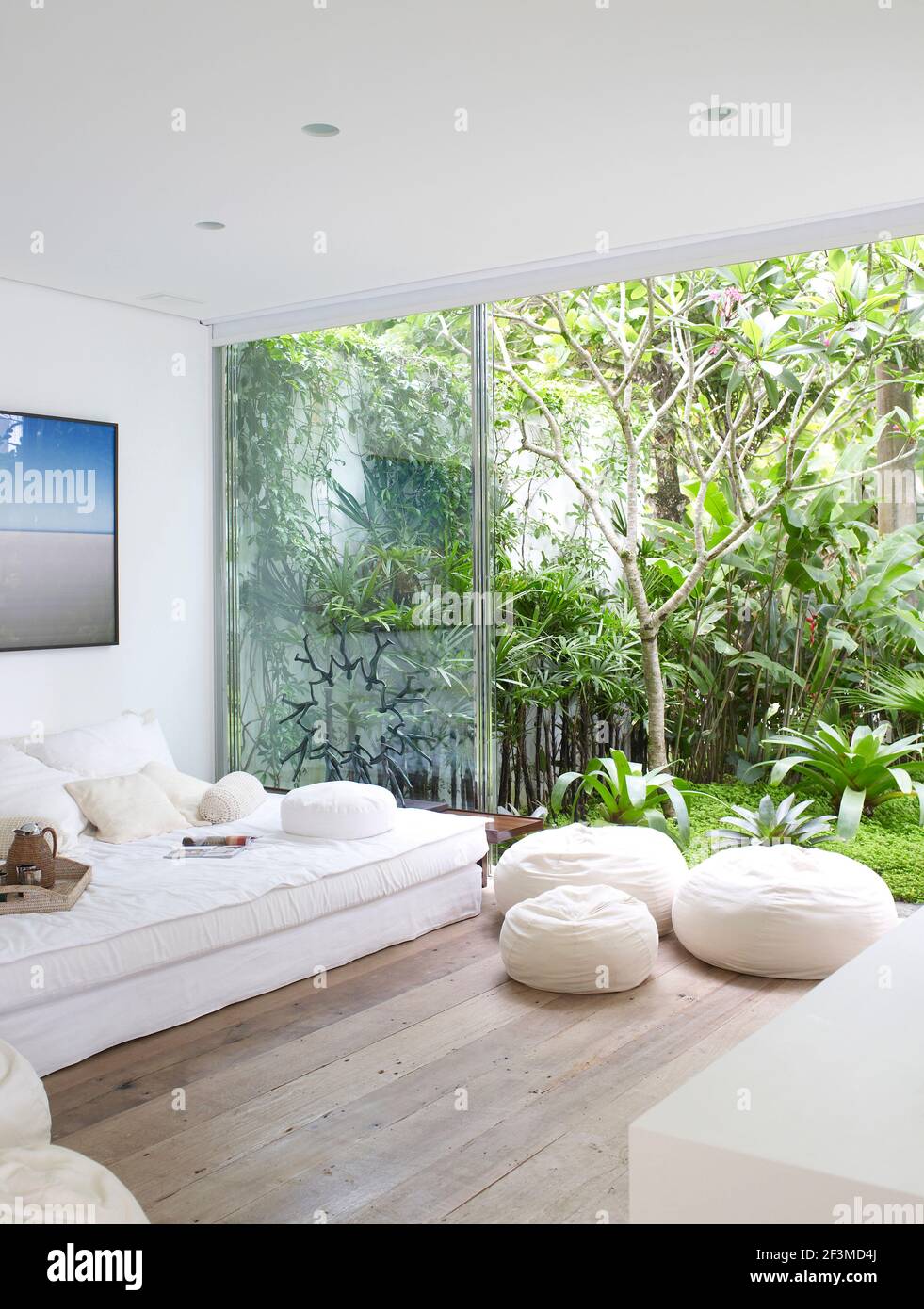 Soggiorno con divani e poufs e vista attraverso con porte a parete aperta in vetro al giardino in casa residenziale, Brasile. Foto Stock