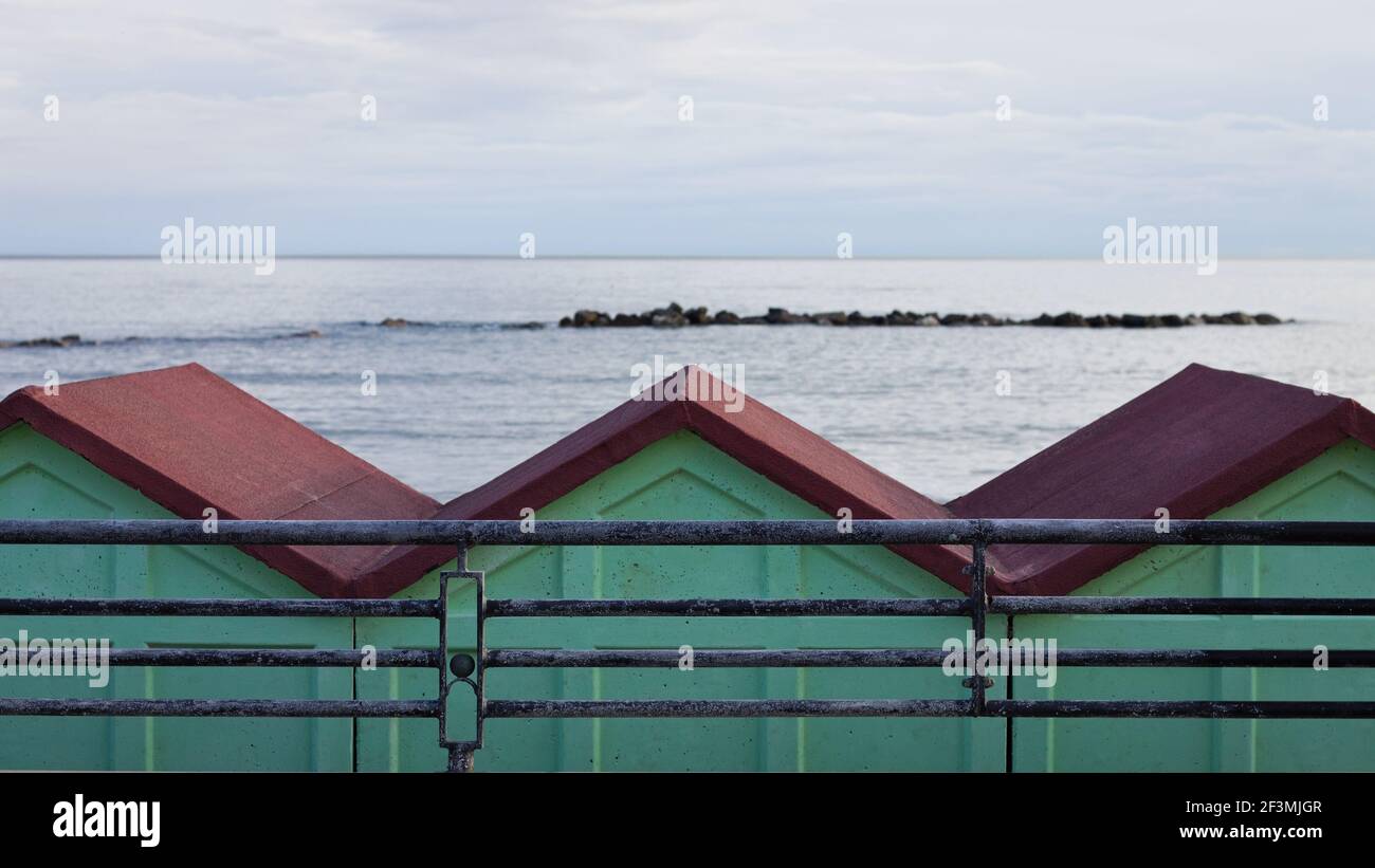 Una serie di cabine da spiaggia rosse e verdi dietro una recinzione in acciaio sulla costa mediterranea di fronte al mare (Pesaro, Italia, Europa) Foto Stock