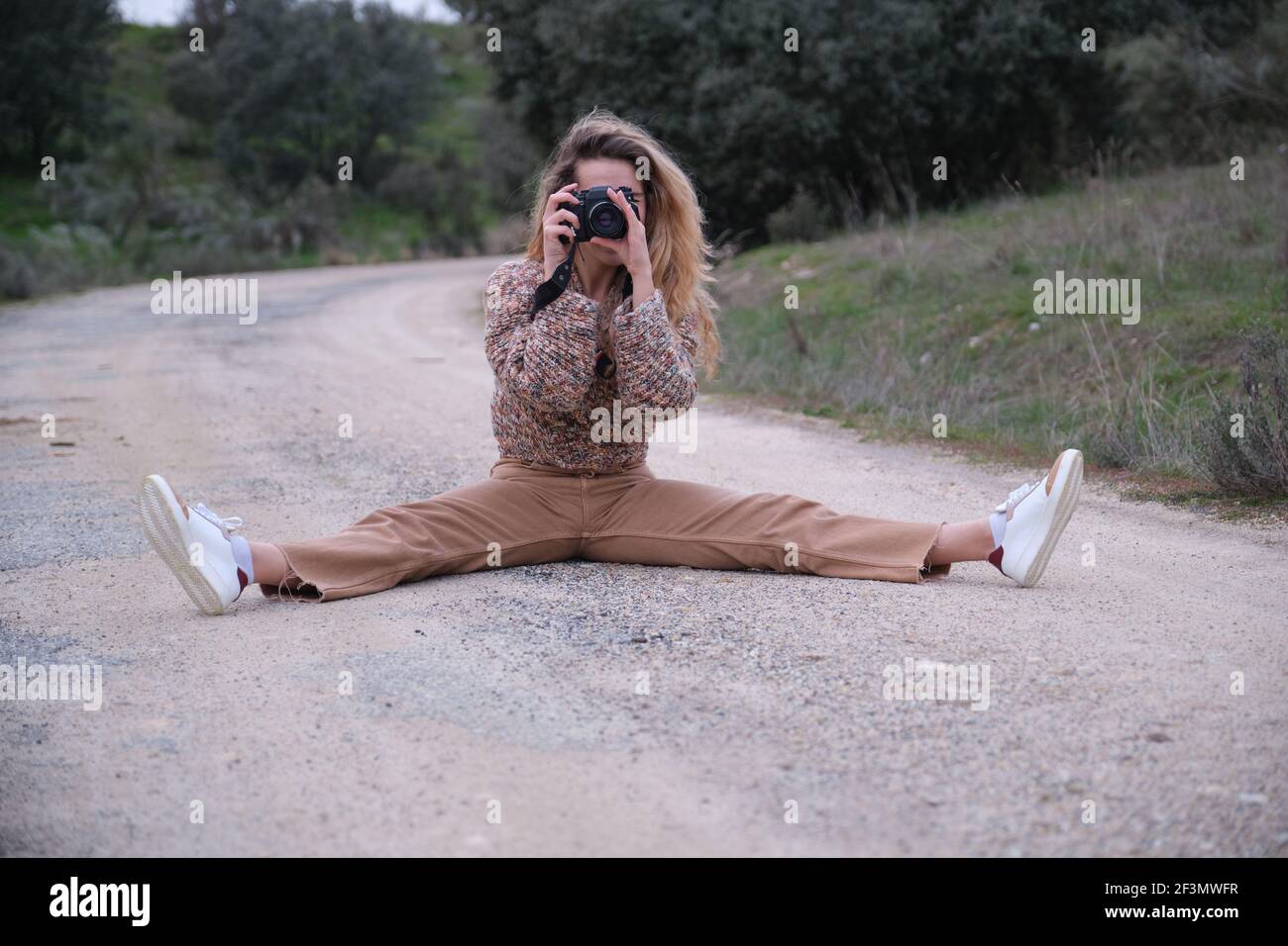 Giovane donna che scatta una foto con la fotocamera su una strada sterrata. Concetto di fotografo. Foto Stock
