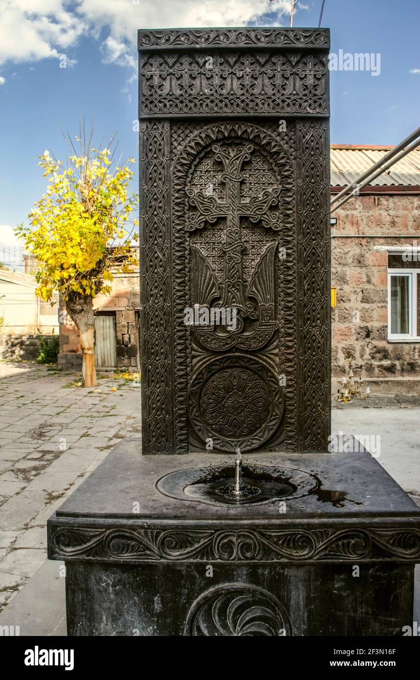 Khachkar scolpito da basalto nero con una fontana da bere memorabile sulla strada vicino a un edificio residenziale in città Di Gyumri Foto Stock