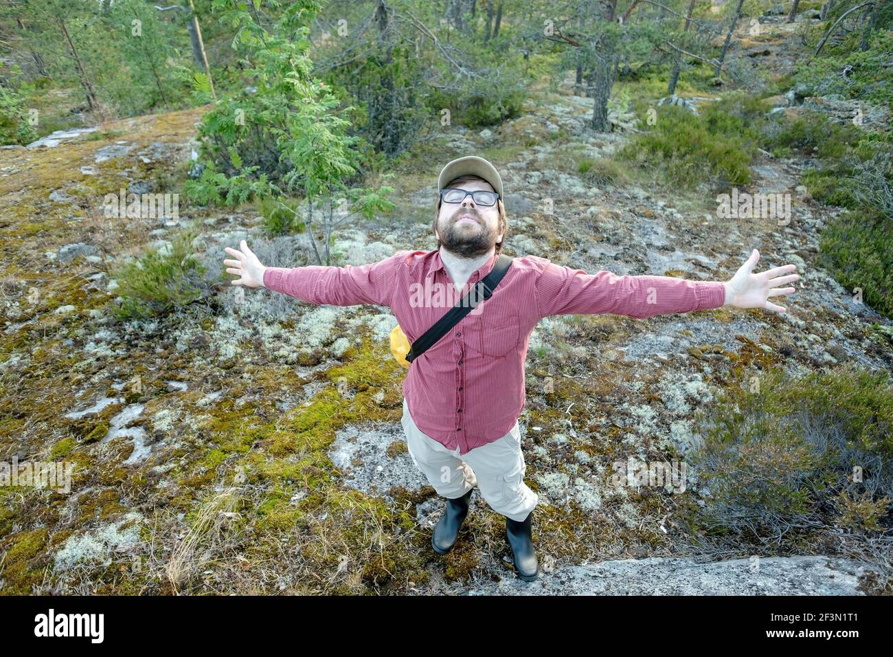 L'uomo soddisfatto ha steso con gioia le braccia ai lati, è in vacanza, camminando nella foresta godendo dell'aria fresca e della natura. Foto Stock