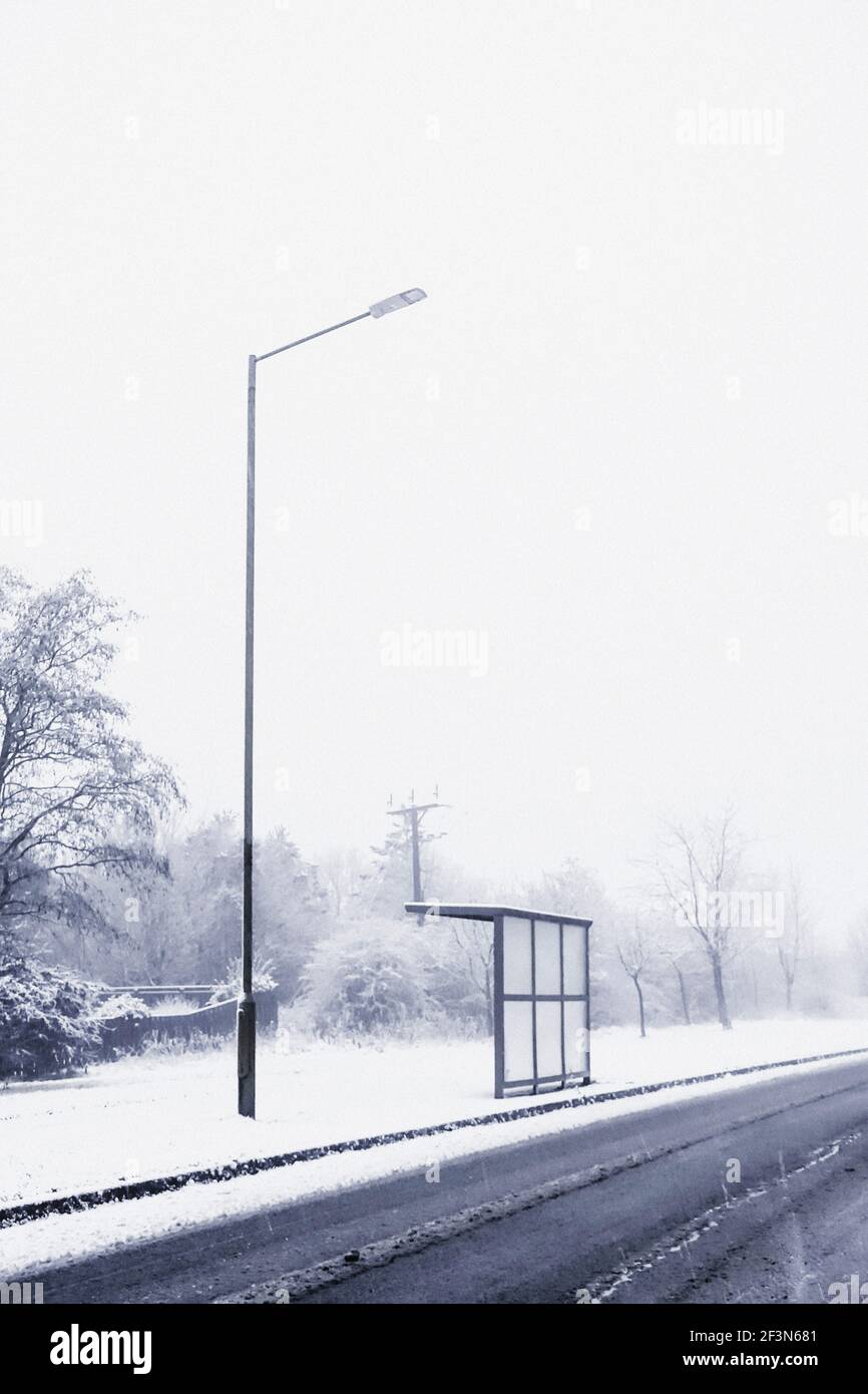 Una fermata dell'autobus e un semaforo su una strada vuota strada in una tempesta di neve Foto Stock