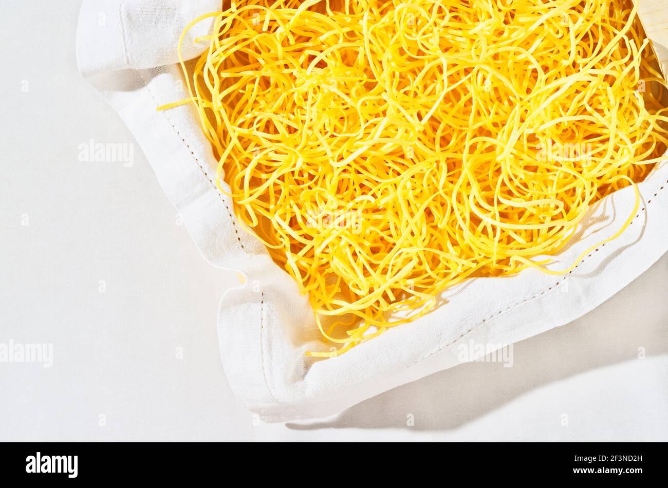 Mucchio di tagliatelle fresche in tovagliolo bianco , bellissimi nastri di pasta cruda lunghi e piatti gialli Foto Stock