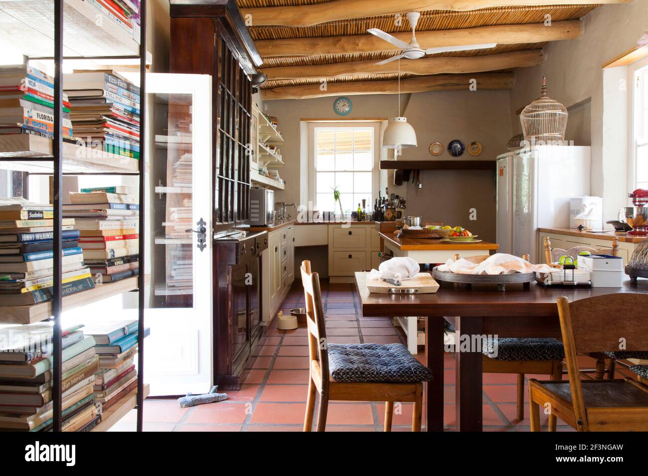 Cucina in stile fattoria con isola cucina, tavolo da pranzo e sedie,  scaffali libro, soffitto a canna e mobili da cucina crema Foto stock - Alamy
