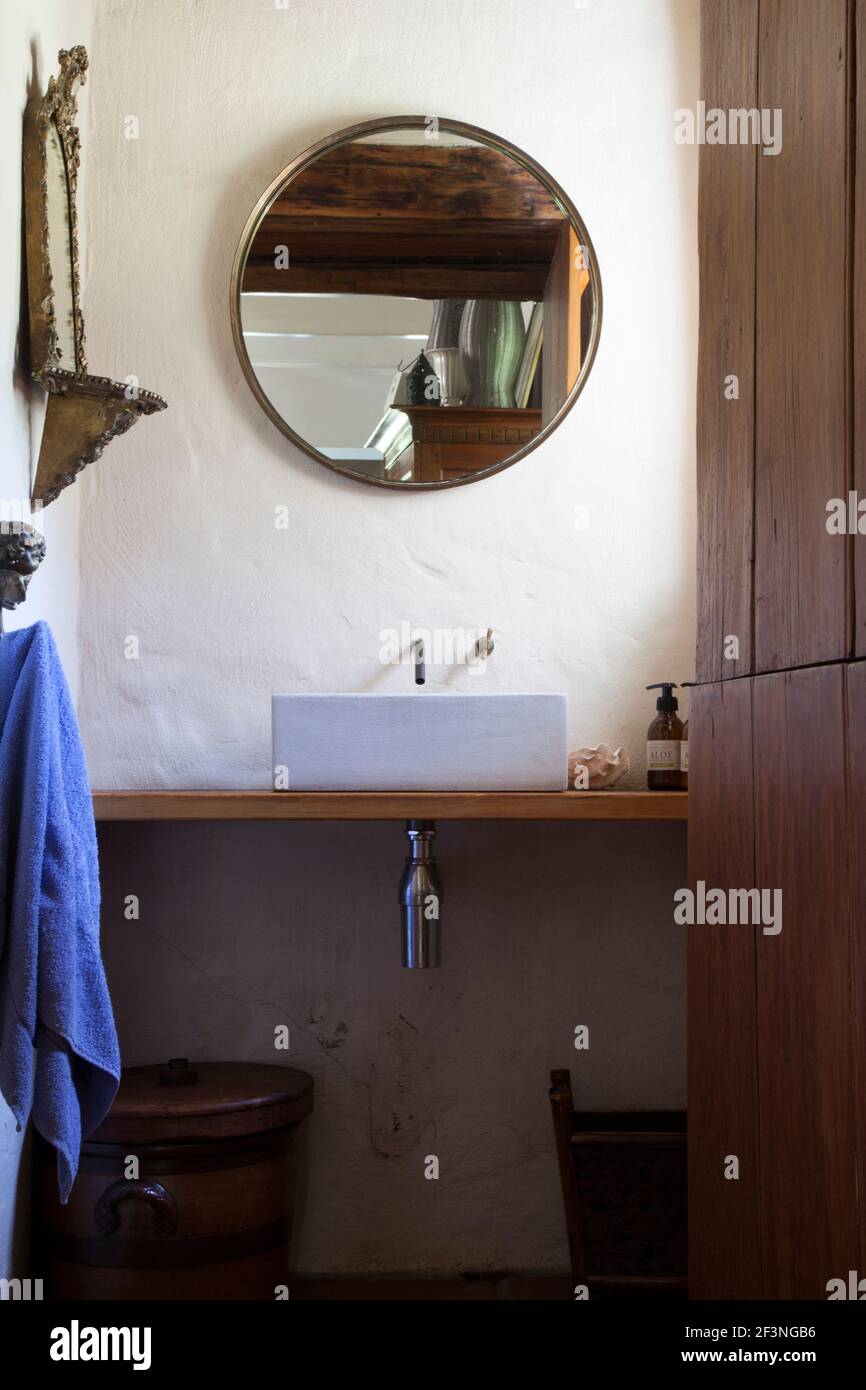 Bagno con lavandino e lavandino in legno con specchio rotondo soffitto in legno riflettente e asciugamano viola appeso Foto Stock