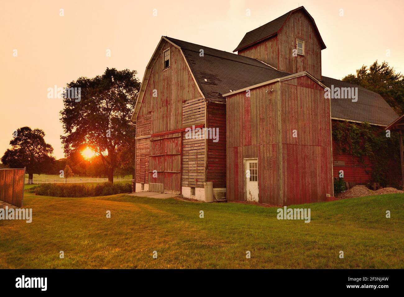 Sycamore, Illinois, Stati Uniti. Un vecchio fienile, intemperie riposa di fronte a uno di una moltitudine di tramonti che è testimoniato sulla sua esistenza. Foto Stock