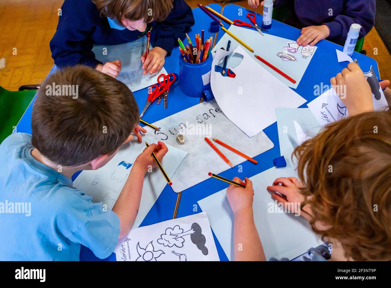 Bambini della scuola primaria che scrivono su una scrivania durante una lezione. Foto Stock