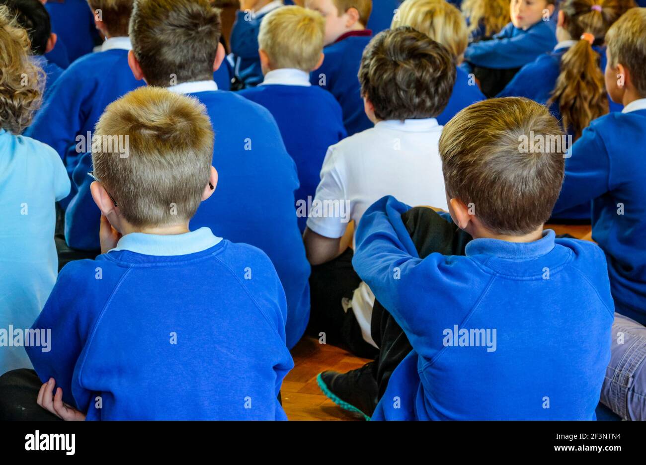 Gruppo di bambini della scuola primaria seduti sul pavimento durante un'assemblea scolastica. Foto Stock