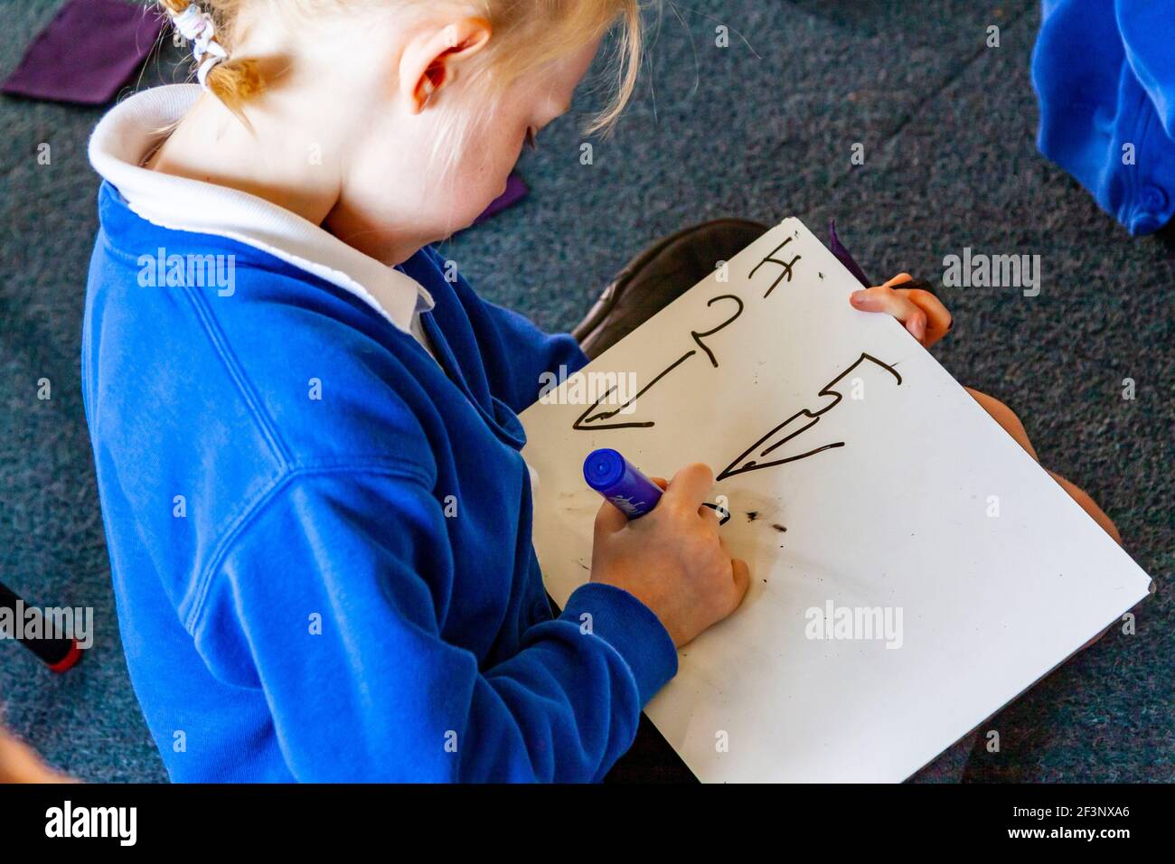 Bambino della scuola primaria che scrive su un bordo pulito della salvietta durante una lezione. Foto Stock