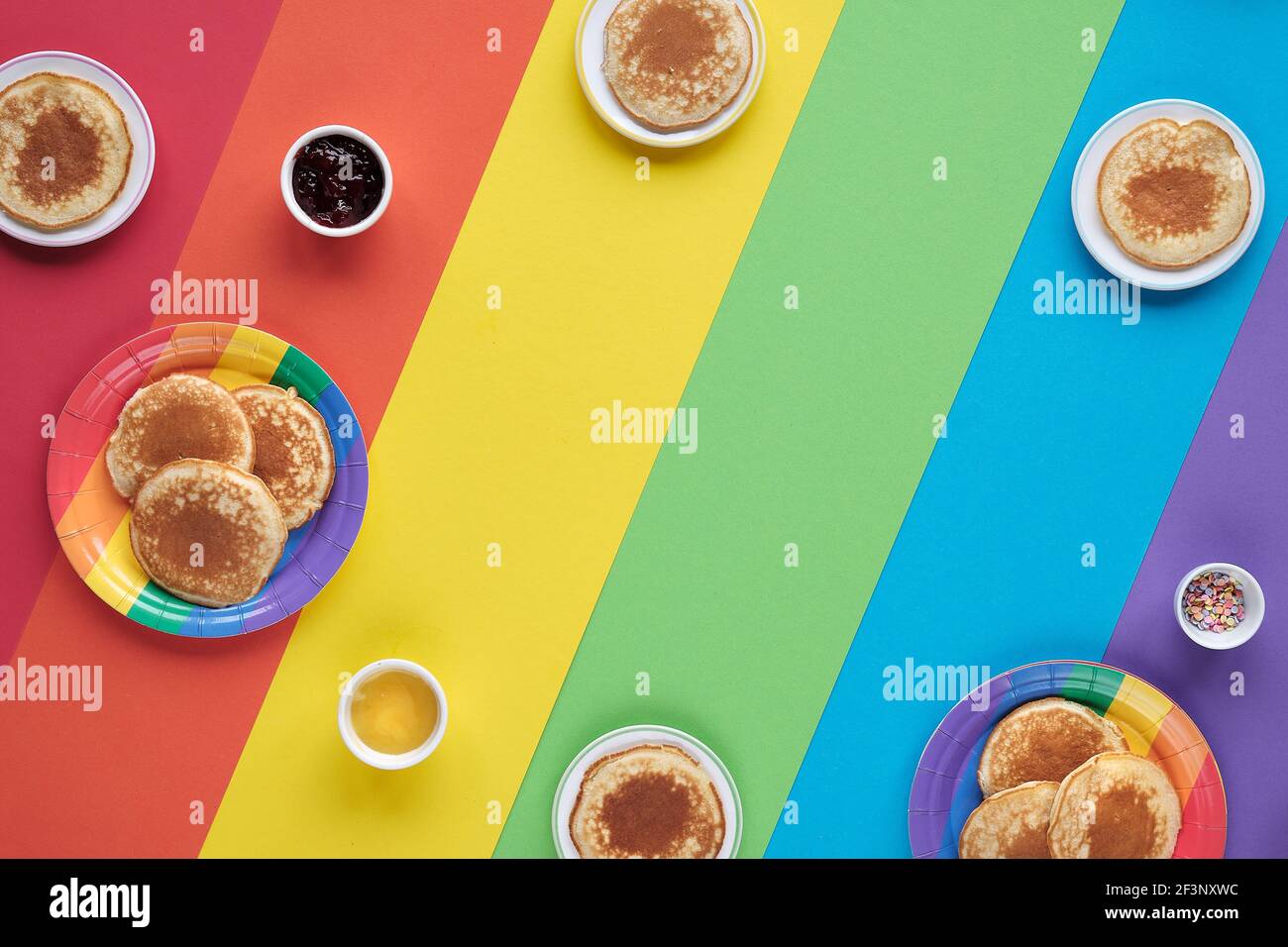 Piccoli pancake rotondi su piatti bianchi e arcobaleno. Disposizione piatta, vista dall'alto su carta color arcobaleno. Spazio-copia, posto per il testo. Foto Stock