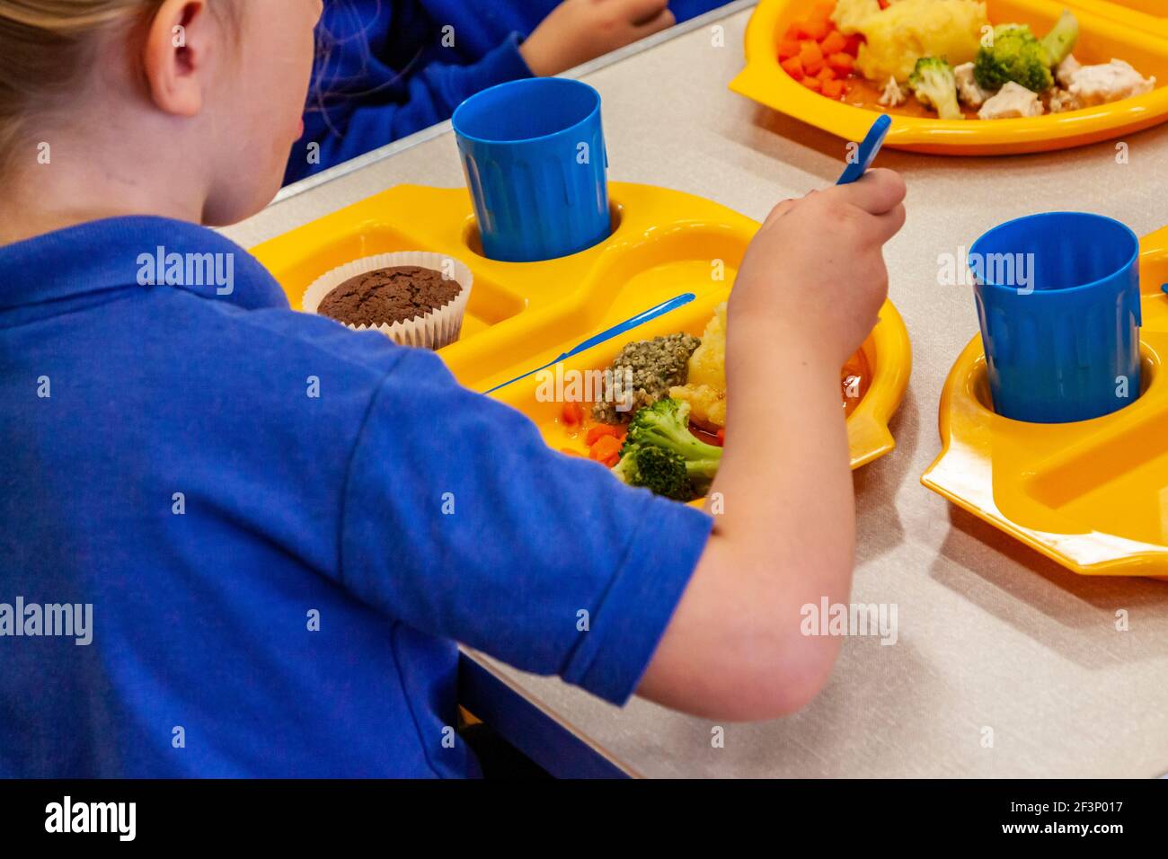 I bambini in una scuola elementare mangiano la cena a scuola usando piatti, tazze e posate di plastica. Foto Stock