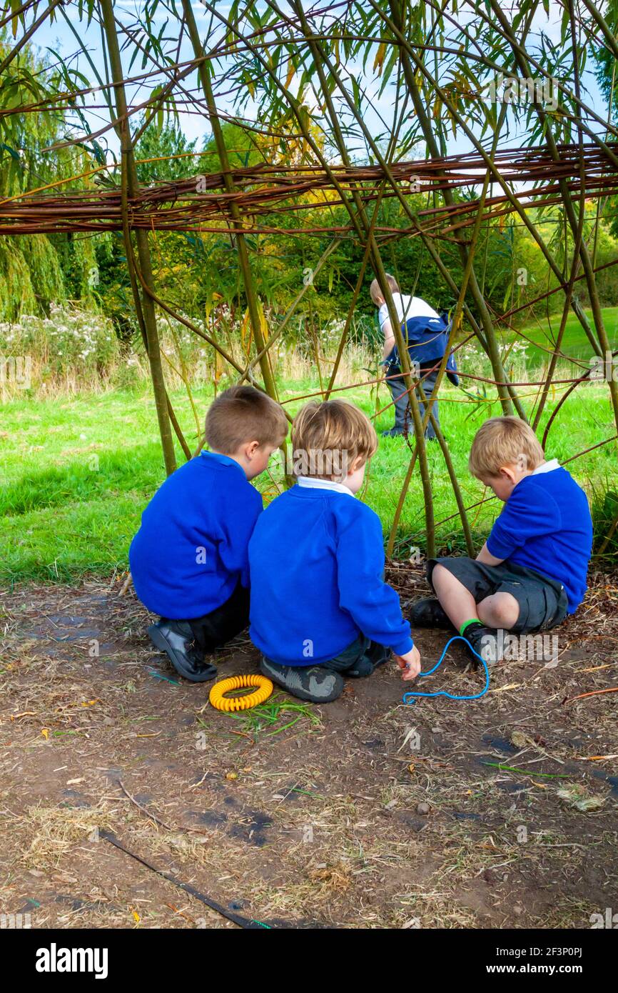Gruppo di bambini della scuola primaria che giocano sotto una cupola del salice in un ambiente di apprendimento all'aperto in un parco giochi scolastico. Foto Stock