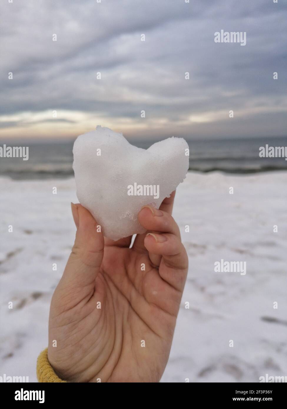 Un primo piano di una mano che tiene la neve a forma di cuore uno sfondo sfocato Foto Stock